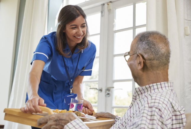 Skilled nurse serving dinner to a senior man at a nursing facility at Booker T. Washington in Shreveport, LA