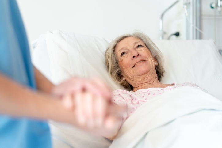 Senior woman lying on bed and female nurse holding her hand during long-term care at Booker T. Washington in Shreveport, LA